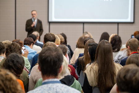 Crowd of attendees listening to speaker during business conference presentation, focused audience,...