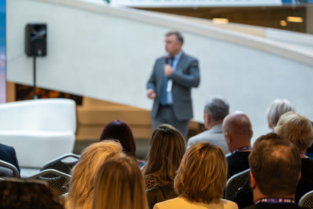 Speaker delivers talk to engaged audience in bright modern atrium at conference. Attentive...