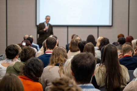 Large audience listening to speaker during professional conference presentation, people seated,...