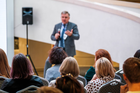 Business speaker engages attentive audience during professional conference presentation, networking and learning atmosphere.の写真素材