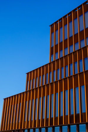 Modern office facade with orange vertical fins and reflective blue windows, geometric repetition and clean architectural lines under clear sky.の写真素材