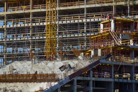 Workers building modern high rise, concrete formwork, scaffolding, tower crane. Industrial...