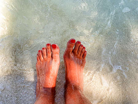 Feet with colored nails of red enamel in the crystal clear sea of the Maldives.の写真素材