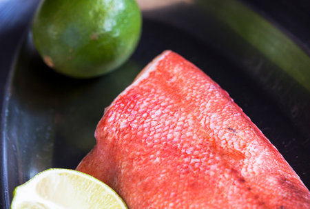 Fresh raw red fish fillet with lime and lemon on black plateの写真素材