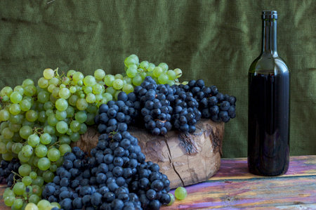 bunch of grapes and bottle of red wine on a wooden tableの写真素材