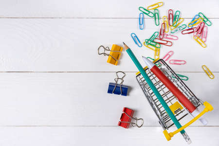 Paper clips in shopping cart on white wooden background