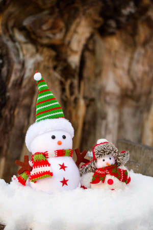 two snowman of fabric stood in the snow on a wooden stumpの写真素材