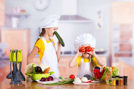two girls having fun in the kitchen with vegetablesの写真素材