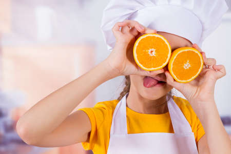 Little girl playing with fresh Mandarin fruits, shows tangerine eyesの写真素材