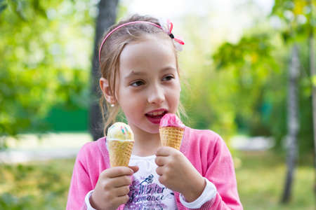 The girl laughs gleefully holds ice cream on a background of green leaves