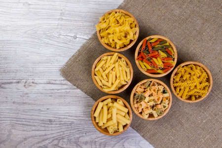 Various mix of pasta on wooden rustic background, sack. Diet and food concept. diversity