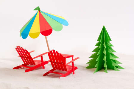 Made from paper Christmas tree, beach chair and umbrella in the sand. White backgroundの写真素材