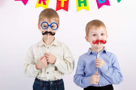 Two boys are holding a carnival mustache and glasses, the inscription happy birthday on a white backgroundの写真素材