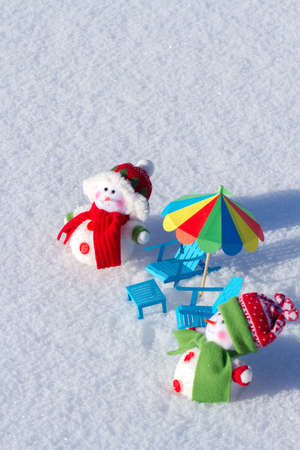 Two cute snowman sunbathing in the snow. Paper chairs and beach umbrellaの写真素材