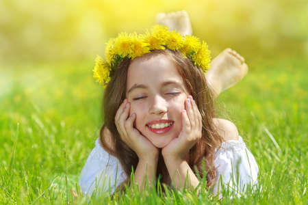 Sweet beautiful girl sitting on a green meadow with dandelionsの写真素材