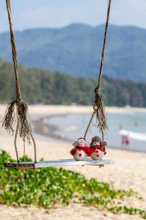 Two cute snowman swinging on a swing in a tropical climate.