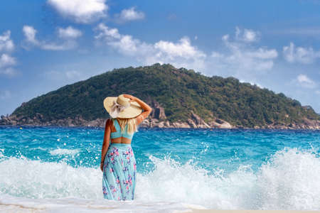 A girl in a blue summer dress with a hat on his head, standing on the white sand. Similan Islandsの写真素材