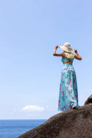 Girl in a blue dress standing on stone and looking into the distance of the horizonの写真素材