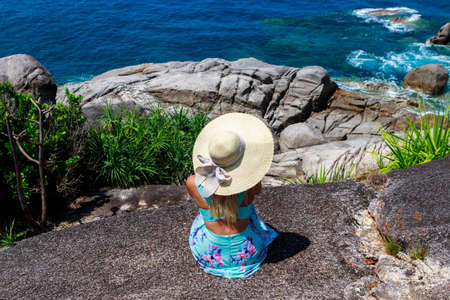 Girl in a blue dress is sitting on stone and looking into the distance of the horizonの写真素材