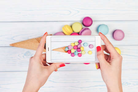 Women's hands holding mobile phone and take pictures of dish from macaroons