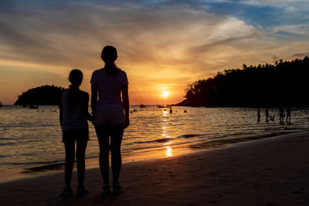 A child and a woman look at the sunset on the beachの写真素材