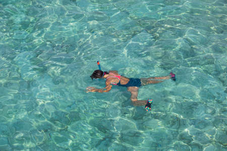 A girl in a diving mask swims in clear water on her stomach. The view from the top.の写真素材