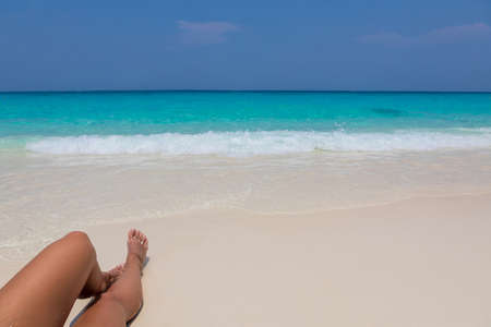 Beautiful female legs stretched out on the sand, beautiful background on the blue water.