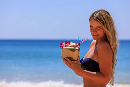 Beautiful girl in a swimsuit with coconut on the beach.の写真素材