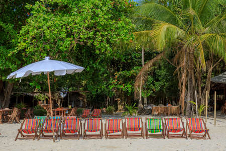 An umbrella and several sun loungers on a beautiful tropical beach and a sea view with a coconut...