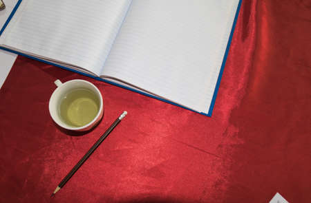 Cup of tea,notebook and pencil on red fabric.の写真素材