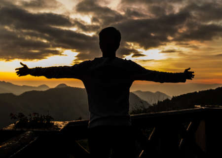 Silhouette of man standing on a mountain in the sunset.の写真素材