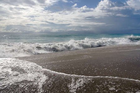 Ocean coast with waves, sand, and cloudy skies