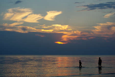Silhouette of two boys in sea at sunsetの写真素材