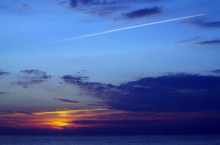 Sea sunset with lighted clouds and an airplane traceの写真素材