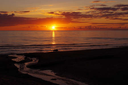Sea sunset with lighted clouds and small river in the foregroundの写真素材