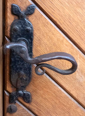 Vintage forged metal door handle on a wooden door closeupの写真素材