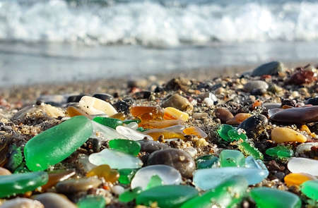 Many wet colored glass polished by the sea on the beach on a blurred background of the oncoming waveの写真素材