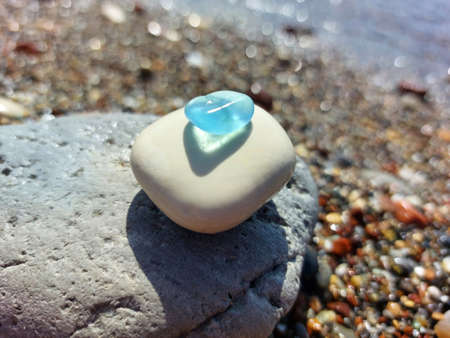 Pyramid of sea stones. A piece of blue glass rolled by the sea lies on top. Blurred background of sand and sea water.の写真素材