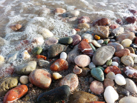 Multicolored sea pebbles close-up in the oncoming waveの写真素材