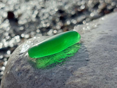 A piece of green glass polished by the sea on a large gray stone on a blurred background on a summer sunny day close upの写真素材