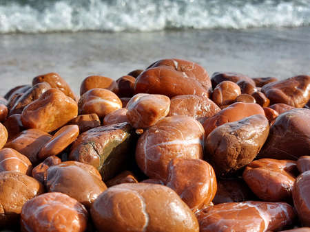 Unique red jasper beach. Many pieces of red jasper polished by the sea. Wet sea stones on a blurred background of the oncoming wave.の写真素材