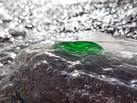 A piece of green glass polished by the sea on a large gray stone in the oncoming wave