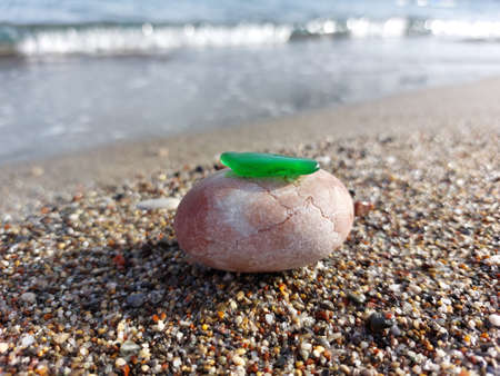 Green glass on a pink stone rolled by the sea on a blurred background of the sea wave on a summer sunny dayの写真素材