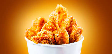 Fried Chicken wings and legs. Bucket full of crispy kentucky fried chicken on brown background. Tasty and juicy deep fried chicken close upの写真素材