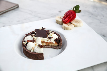 Chocolate tart with strawberries and banana on a white marble table.の写真素材
