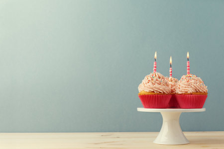 Sweet garnished cupcakes with burning birthday candles on blue backgroundの写真素材