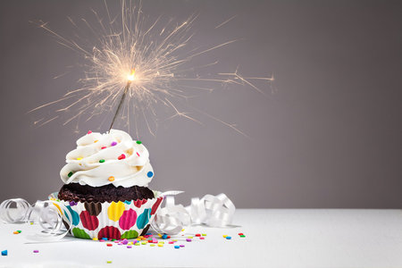 Cupcake with colorful sprinkles and a sparkler over a grey backgroundの写真素材