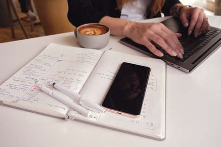 Beautiful lady is drinking coffee while working on a laptop in a coffee shop. Sunny day