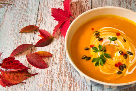 Pumpkin soup with roasted seeds and the sour cream on the wooden table, decorated with autumn leavesの写真素材