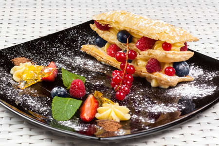 Millefeuille with berries and caramel custard on a dark plateの写真素材